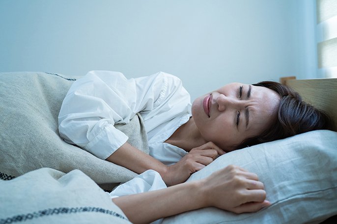 写真:肩の痛みを我慢しながら寝る女性