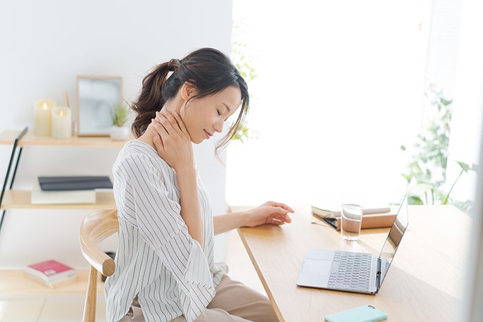 写真：パソコン作業をしている女性が、右首に右手を当てながら下を向いている様子