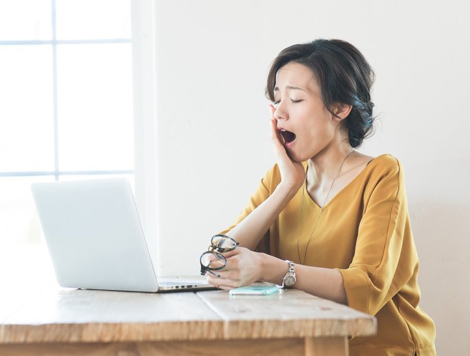 写真：パソコン作業をしている女性が、あくびをしている様子