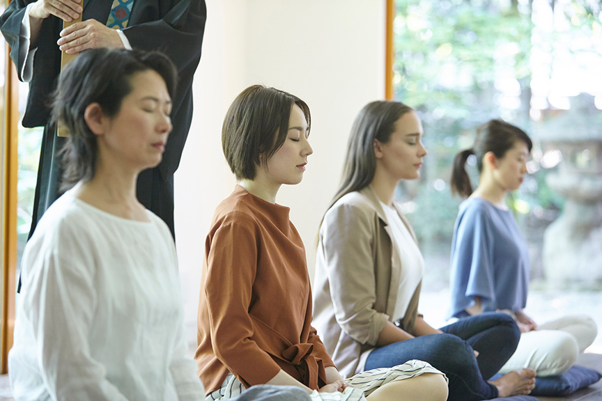 写真：室内で4人が並んで座り、静かに瞑想を行っている様子。