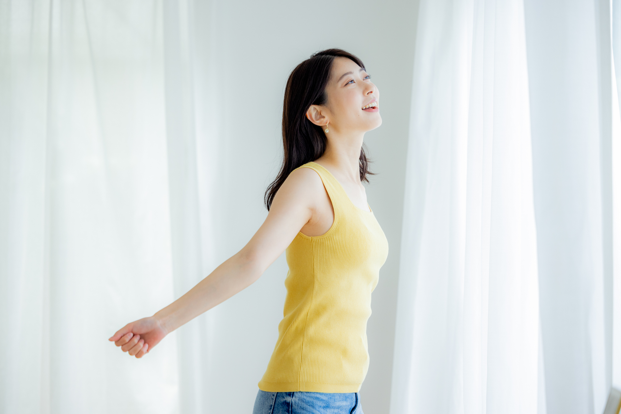 窓の外に向かって笑顔で立っている女性