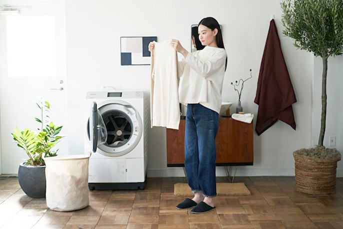 写真：ロングヘアーの女性が洗濯機から洗濯物を取り出して広げて確認してるイメージ