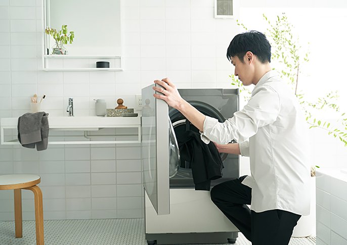 写真：男性が洗濯機に服を入れてるイメージ