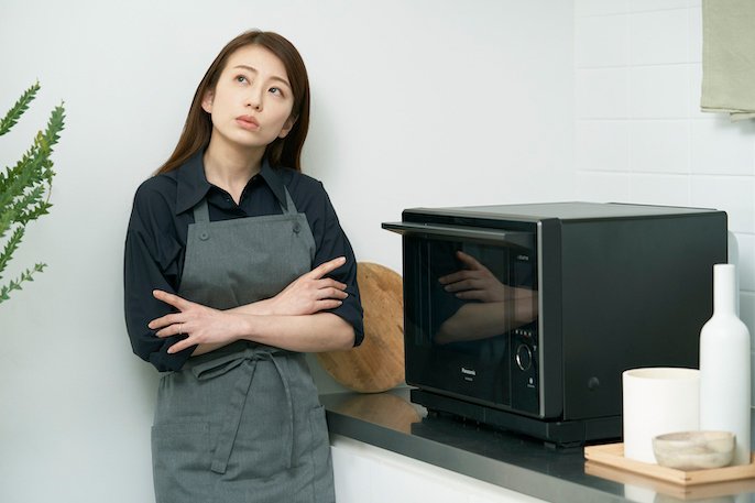 写真：女性がオーブンレンジの前で考えている様子