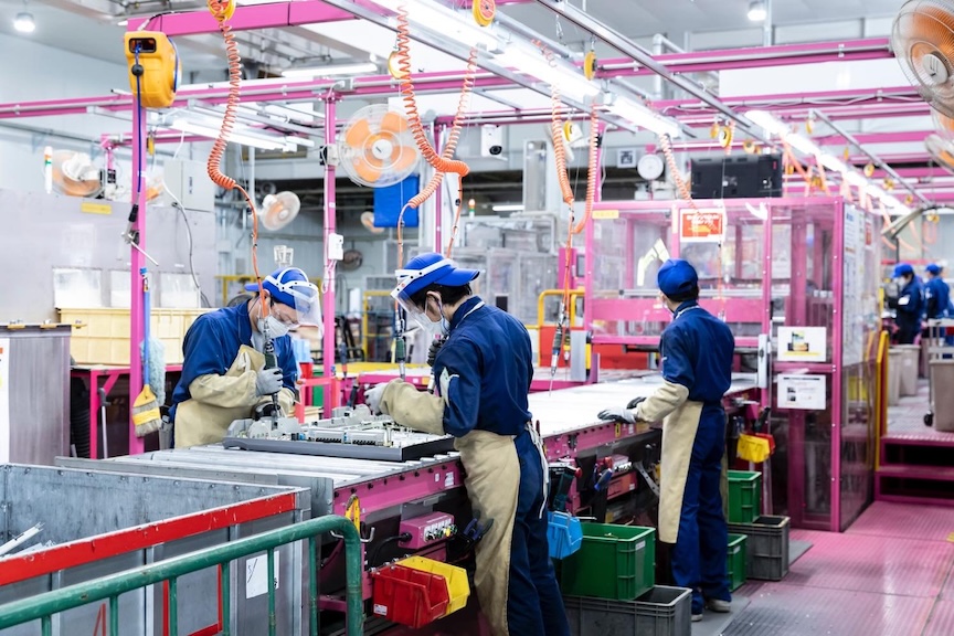 カラフルな設備の中で作業着姿の人が作業している写真