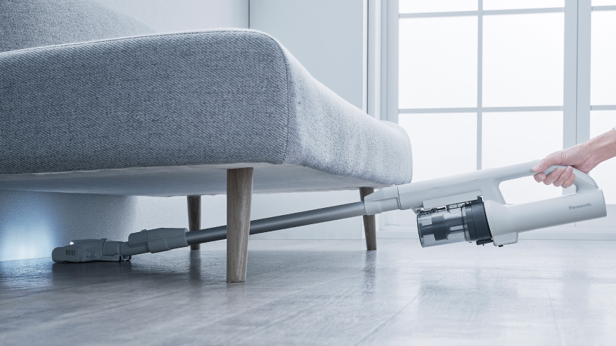 掃除機でソファの下を掃除している写真