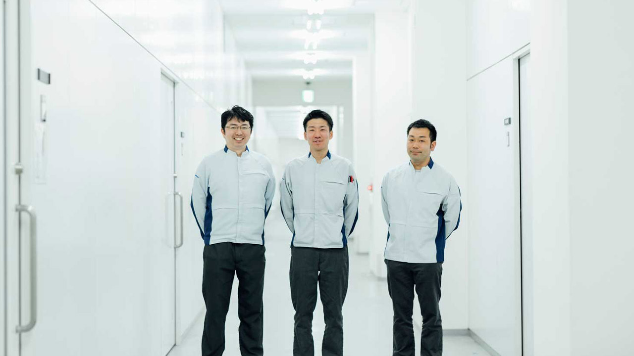 笑顔で立つ作業着姿の3人の男性の写真