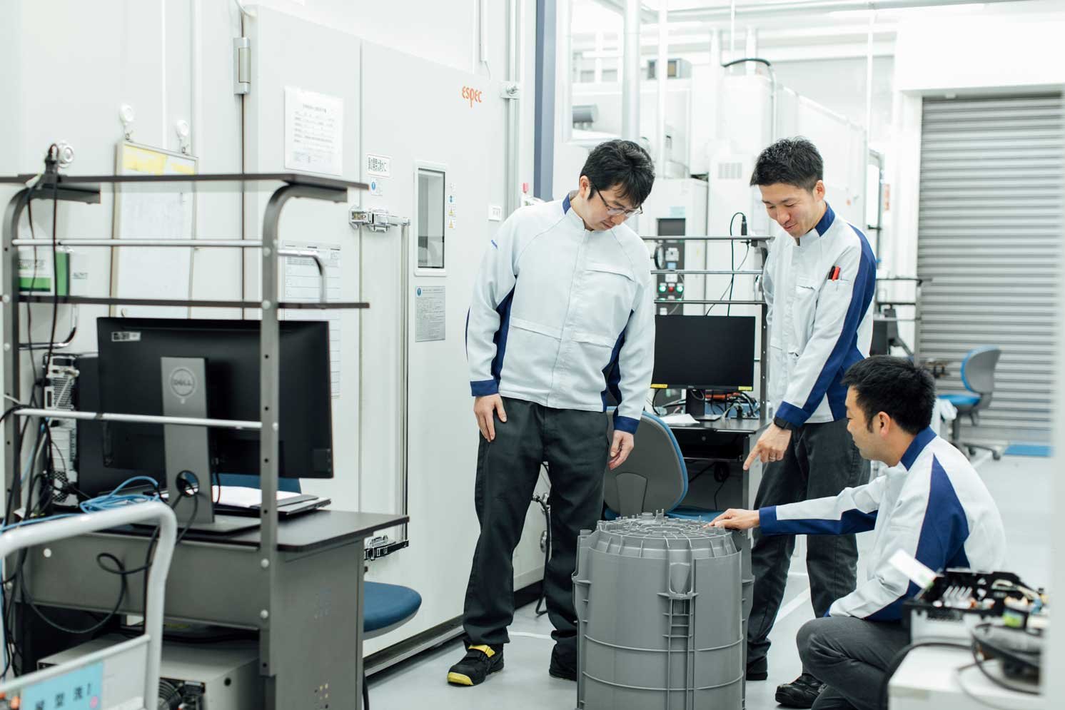 再生プラスチックが使用されている部品を見ている3人の写真