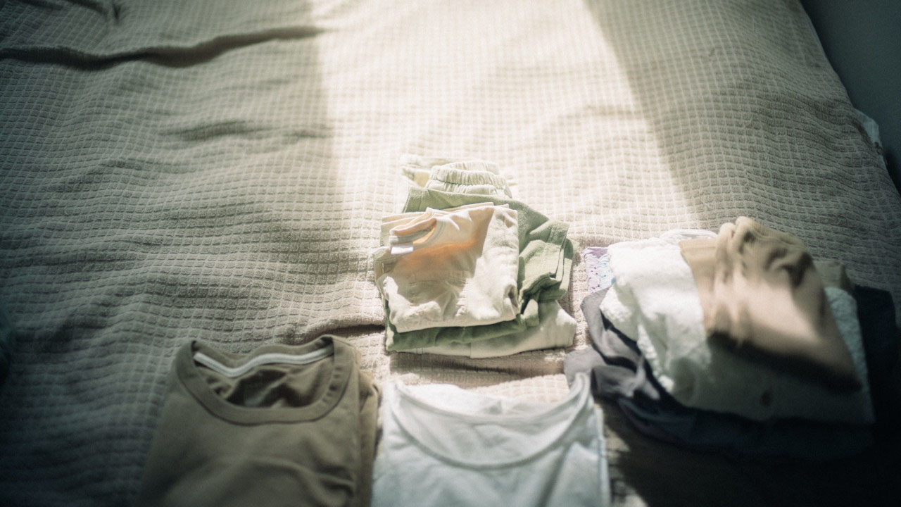 ベッドの上に、畳まれた衣類がいくつか並べられている様子。