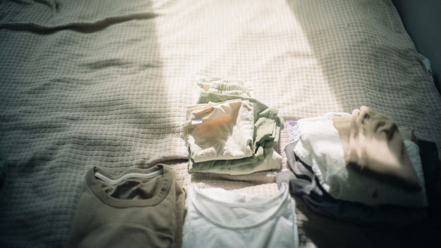 ベッドの上に、畳まれた衣類がいくつか並べられている様子。