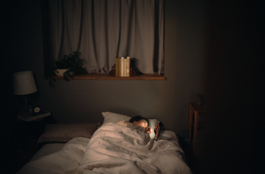 写真：寝室で女性がスマホを見ているイメージ