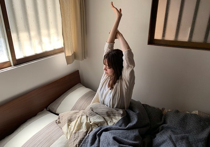 写真：女性が寝起きで腕を伸ばして伸びをしてるイメージ