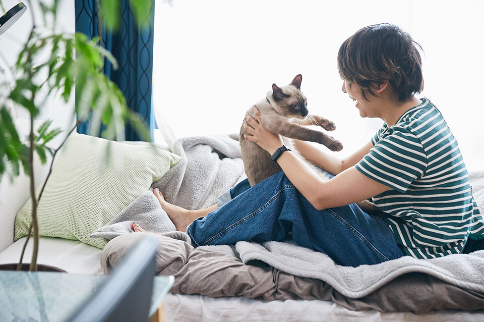 ベッドの上で猫を抱っこする女性