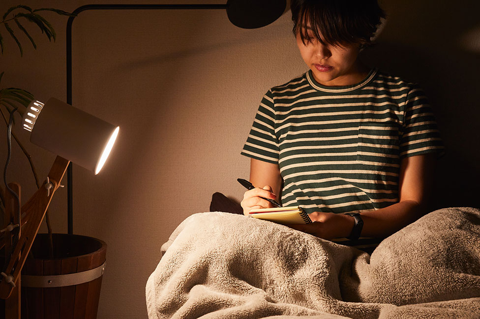 ベッドを照らすLED電球『プレミアX』。ベッドの上でメモする女性