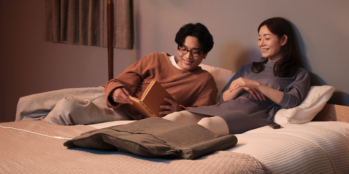 写真：ベッドに横たわって本を見ている男性と女性