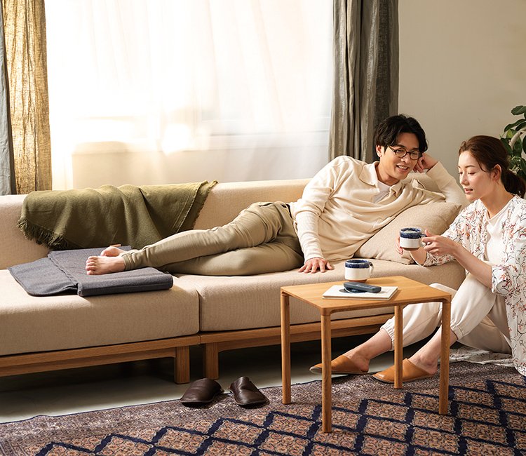 写真：ソファに横たわる男性と床に座ってマグカップを持つ女性