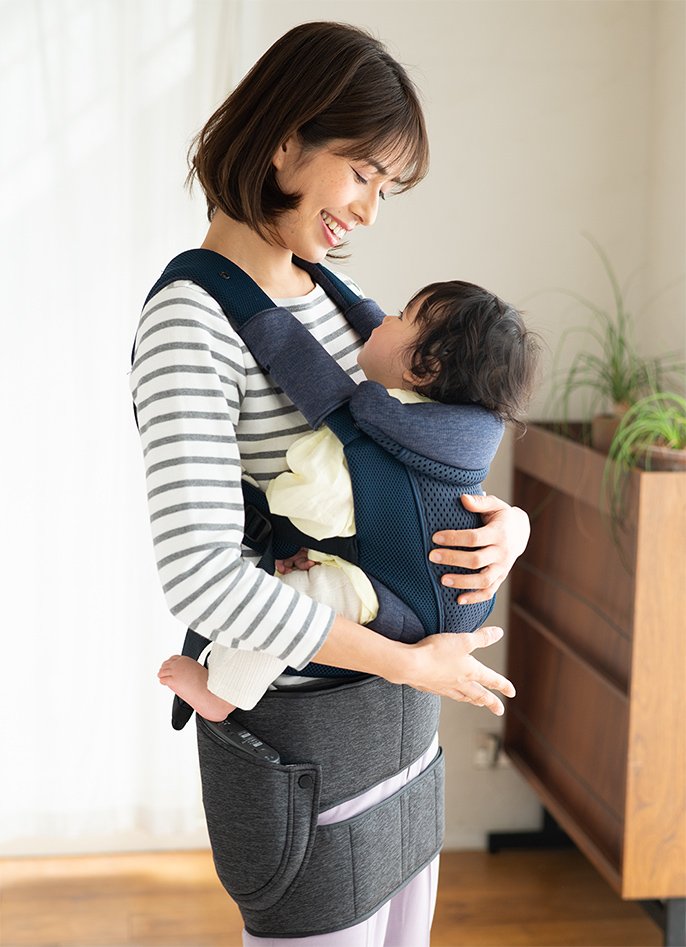 写真:エアーマッサージャーを付けた女性が、赤ちゃんを抱っこしながら笑顔で話しかけている様子