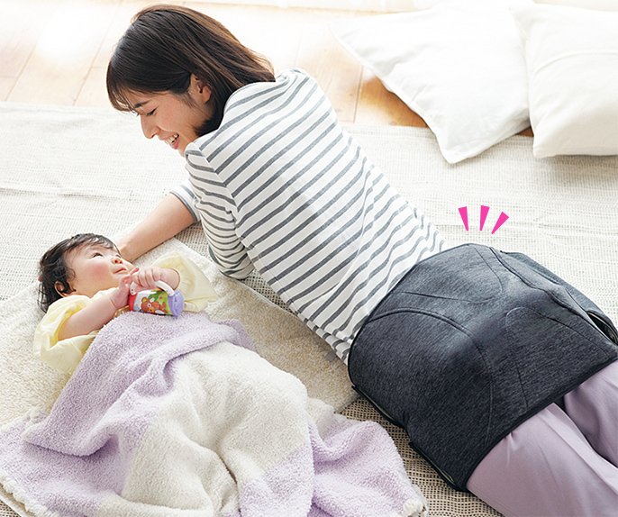 写真:エアーマッサージャーを付けた女性が横になって、赤ちゃんを寝かしつけている様子。