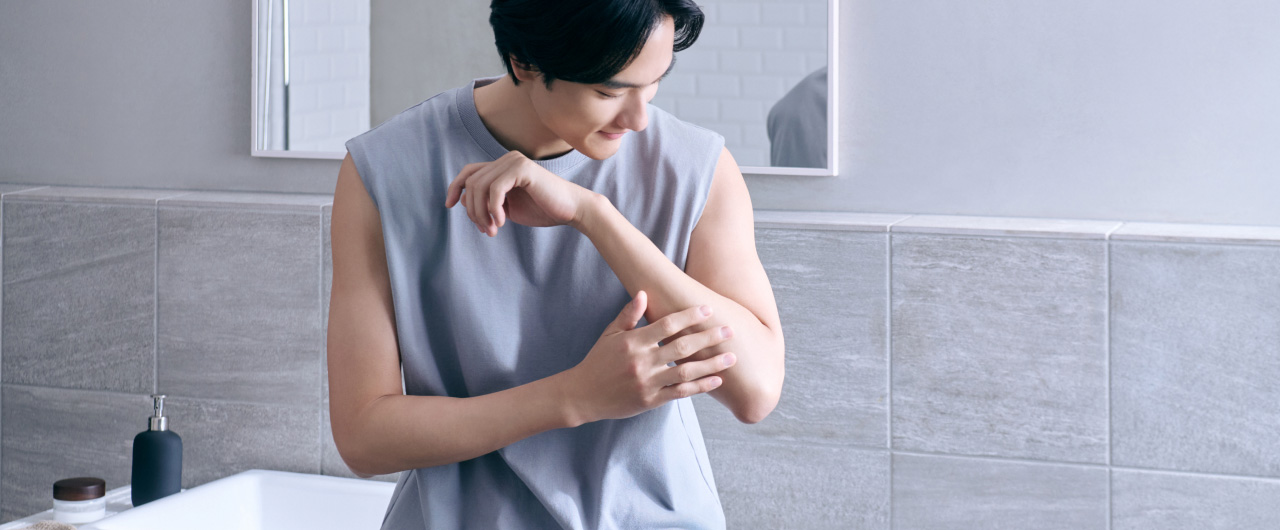 写真：洗面所で腕の肌を手で触れてケアしている人の様子