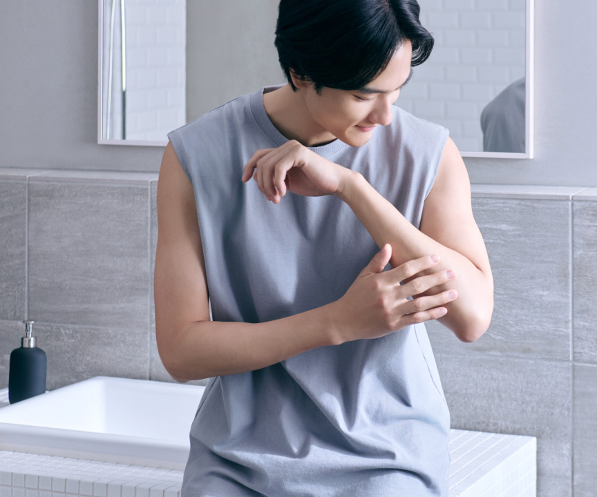 写真：洗面所で腕の肌を手で触れてケアしている人の様子