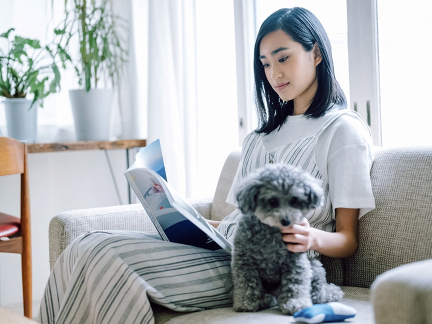 ソファに座って雑誌を開く人の画像です。手前に犬がいます。