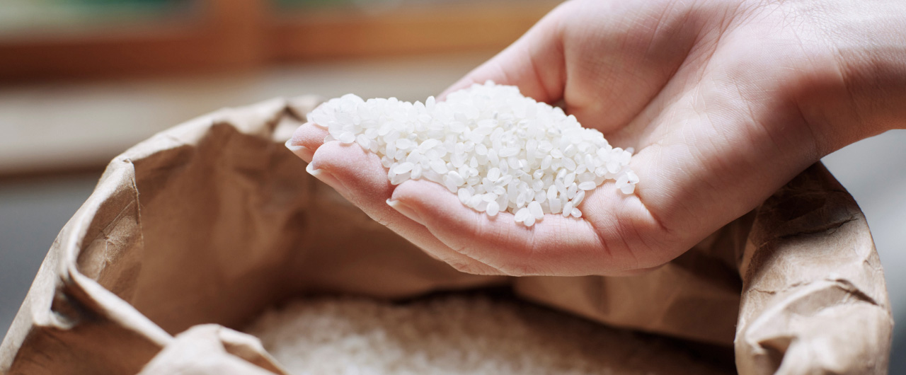 写真：茶色の紙袋に入った白米を、手で一握りすくい上げている様子。