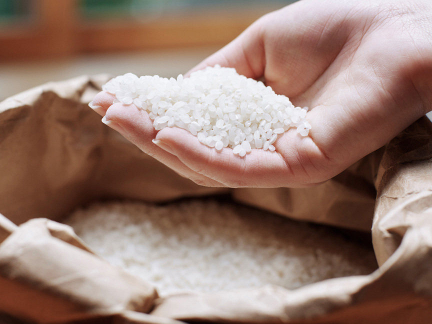 写真：茶色の紙袋に入った白米を、手で一握りすくい上げている様子。