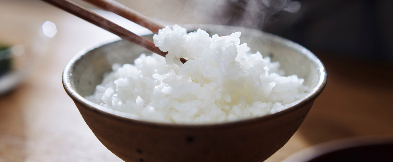写真：湯気の立つ白ご飯を箸で持ち上げた様子