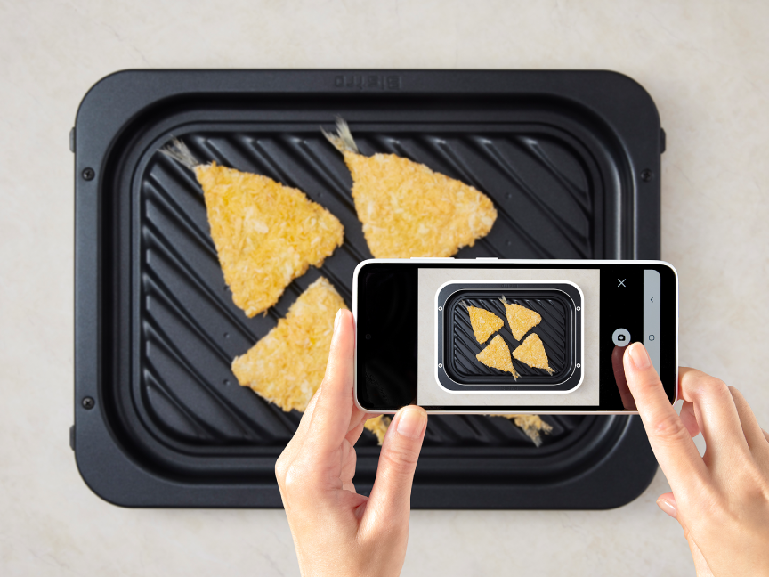 ヒートグリル皿の上に乗せた冷凍フライを、スマートフォンで撮影している様子。