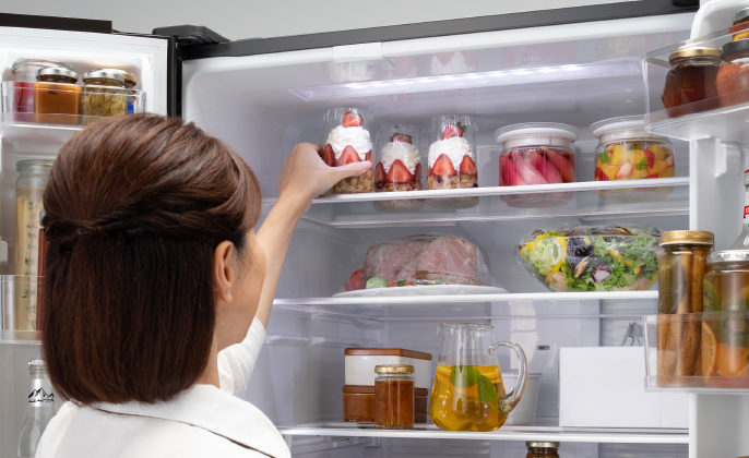 女性が冷蔵室最上段のから食材を取ろうとしている写真です。