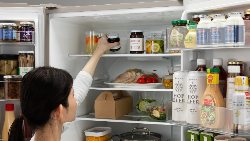 女性が冷蔵室の最上段から食材を取ろうとしている写真です。