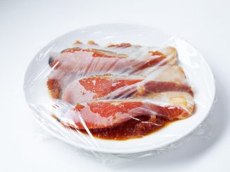 ラップで包まれている、皿の上にのせた魚の画像です。