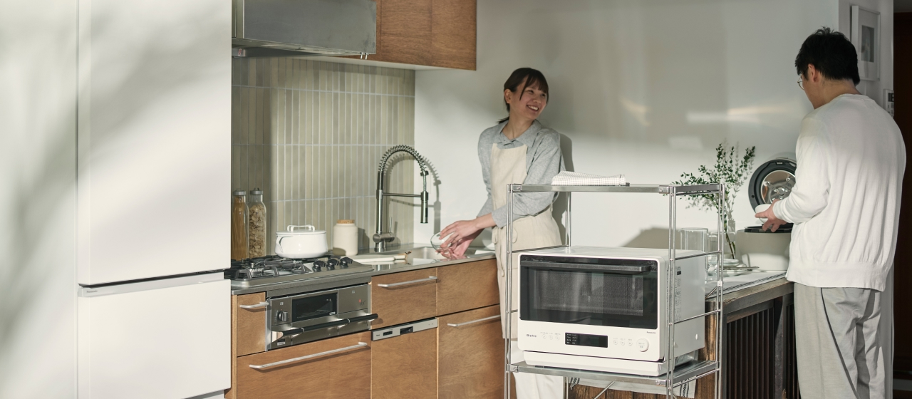 CV:白い家電を置いたキッチンで作業する2人（冷蔵庫・電子レンジ・炊飯器）