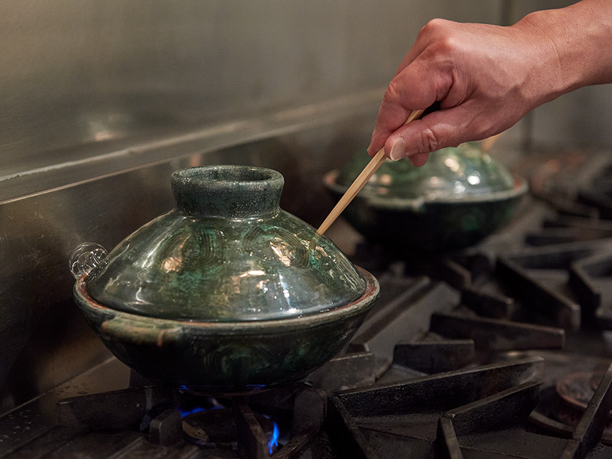 蒸気を逃がさないように、⼟鍋の蓋の⽳を箸でふさいでいる画像です。