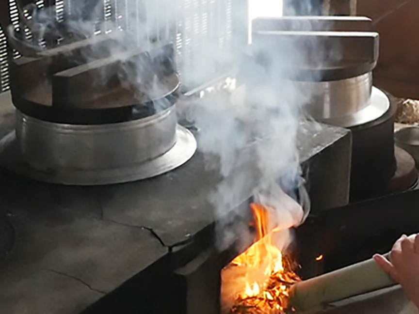 かまどの前で、女性がかまどに空気を送っている画像です。