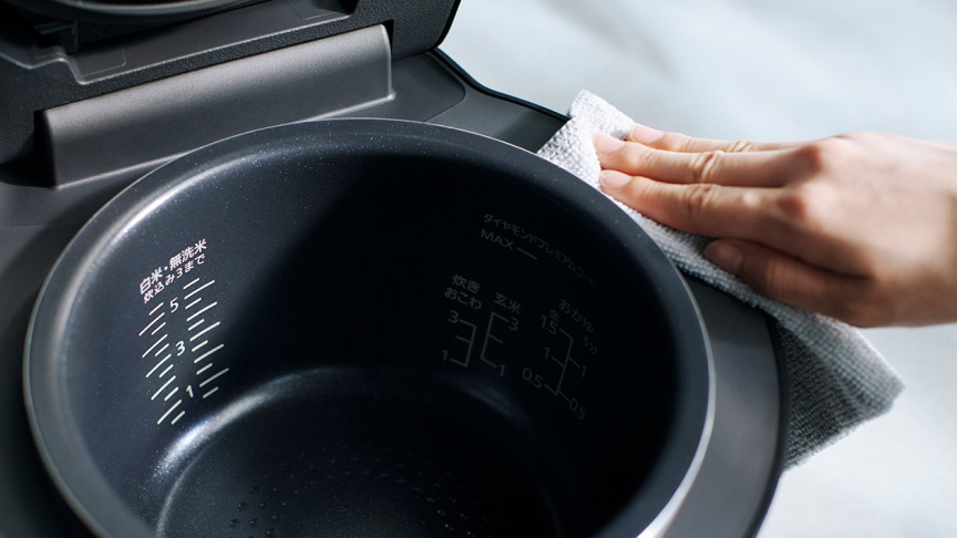 写真：蓋の空いた炊飯器の内釜周りを拭き掃除するようす