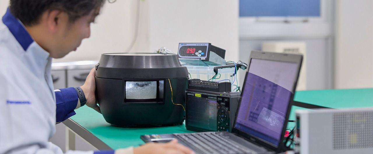 写真：炊飯器とパソコンに向かう大村さん