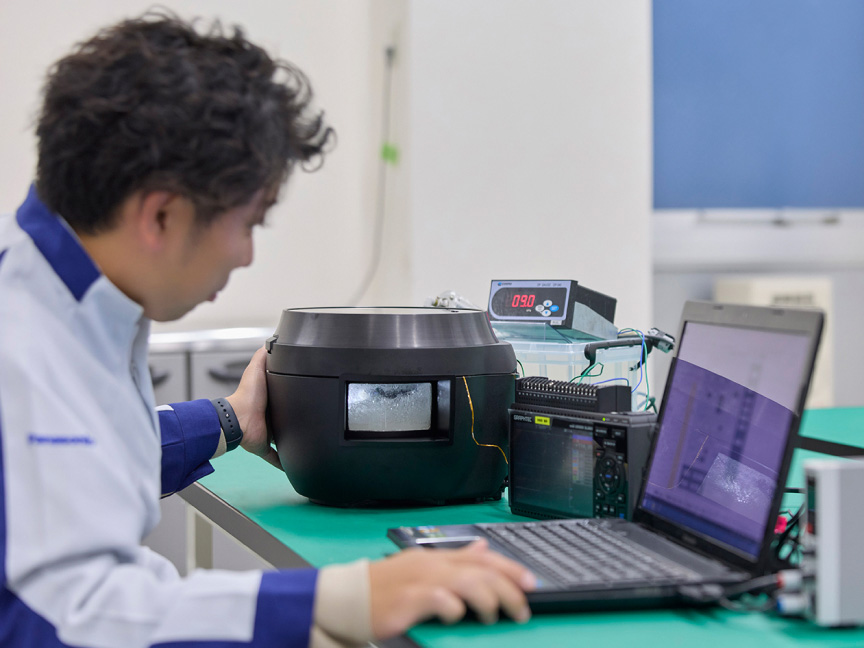 写真：炊飯器とパソコンに向かう大村さん