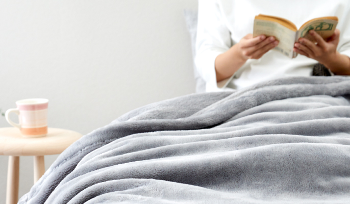 イメージ：ベッドに座り、毛布を脚にかけて読書をする様子