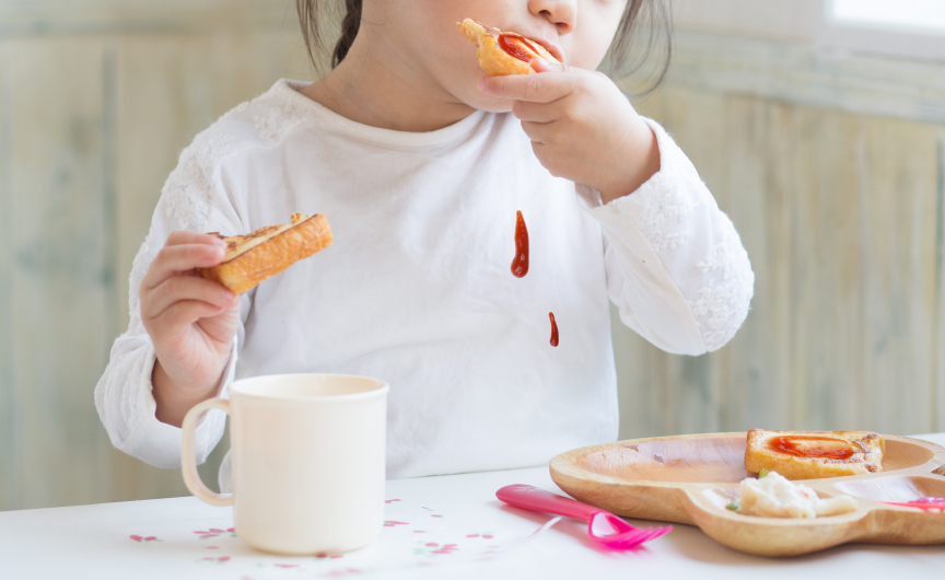 イメージ：子どもが食事中にケチャップをこぼして洋服につけている様子