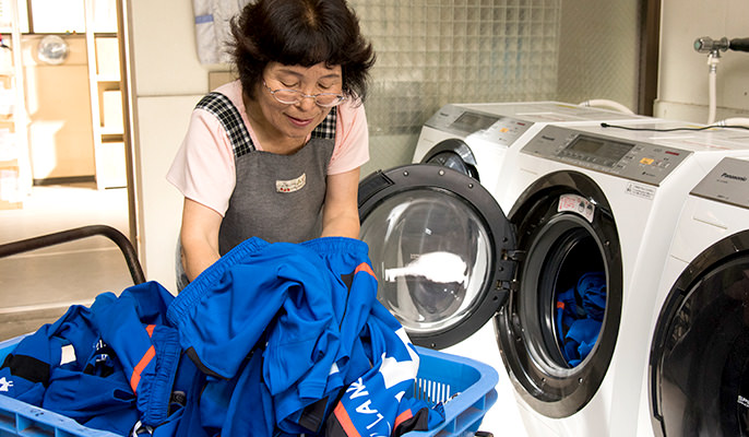 洗濯機にユニフォームを入れている河田の画像です。